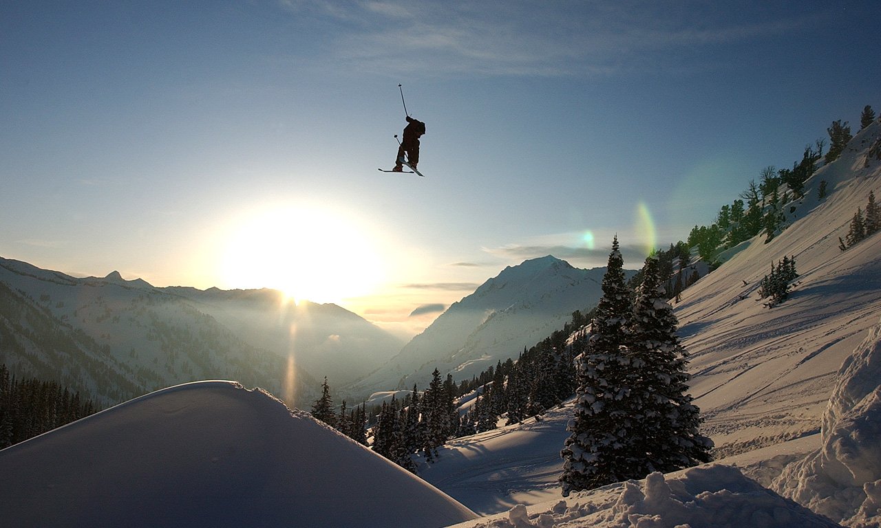 A skier gracefully jumps against a stunning backdrop of snow-covered mountains and a glowing sunrise, capturing the thrill of skiing in winter sports.