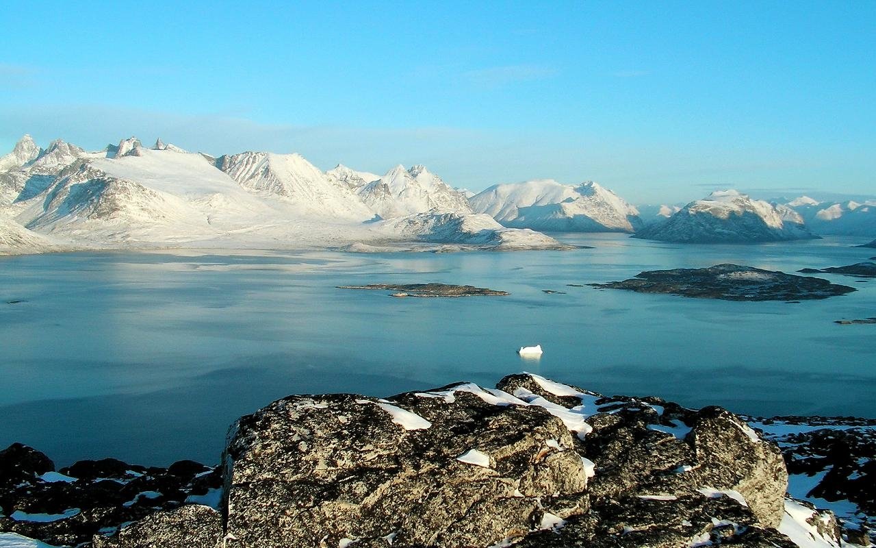 A stunning view of a snowy island surrounded by calm waters, framed by majestic mountains under a clear blue sky, showcasing the beauty of nature.