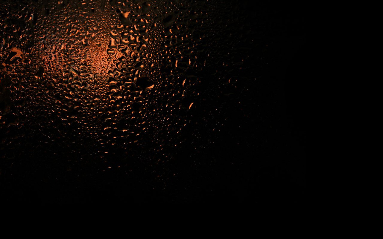 A close-up photography of water drops on a surface, with a warm orange glow illuminating the droplets against a dark background.