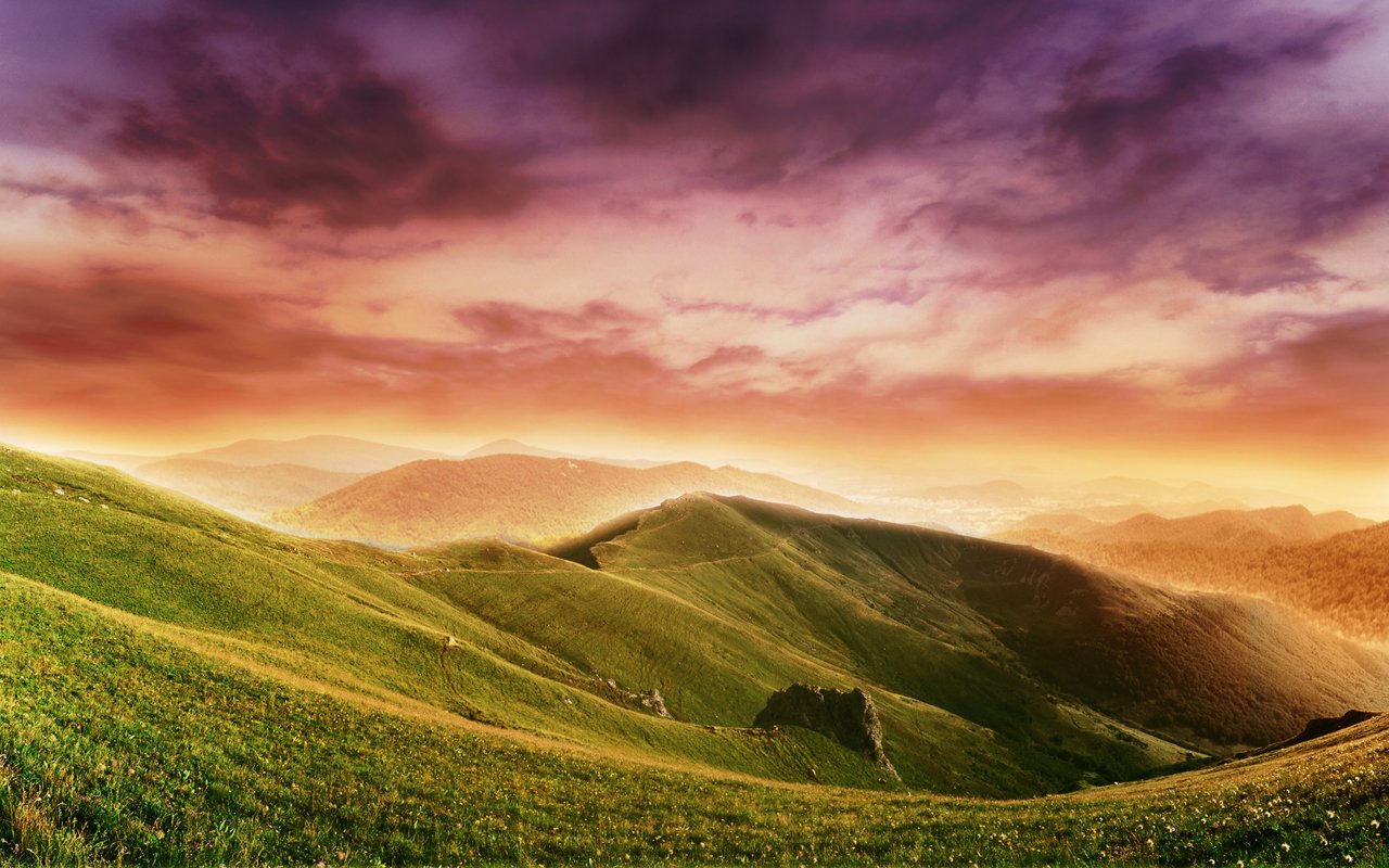 A vibrant sunset illuminates rolling green hills, creating a serene landscape that beautifully showcases nature's tranquility in an expansive field setting.