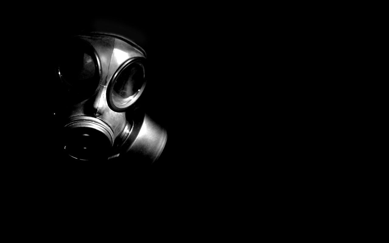 A gas mask emerges from a dark background, its metallic surface and distinct lenses creating a stark contrast against the shadows, evoking a sense of mystery and unease.