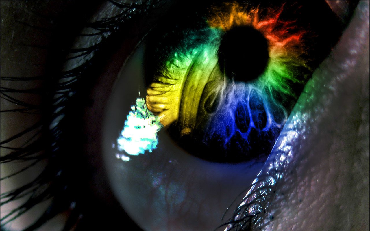 A macro shot of an artistic eye displaying vibrant colors—green, yellow, and blue—reflecting a striking, multi-colored iris and intricate details.