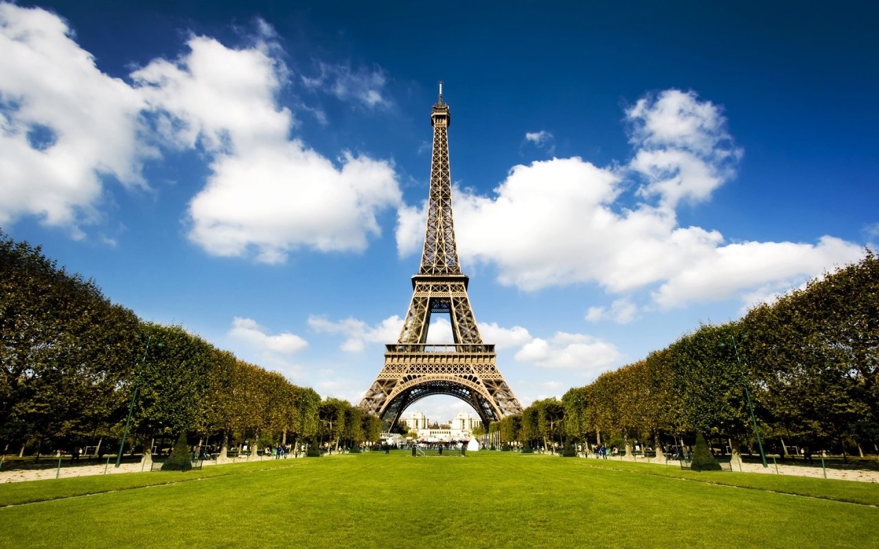 The Eiffel Tower stands majestically in Paris, framed by lush greenery and a bright blue sky, showcasing its iconic man-made structure.