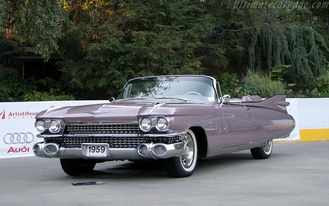 1959 Cadillac convertible vehicle parked outdoors with lush greenery in the background.