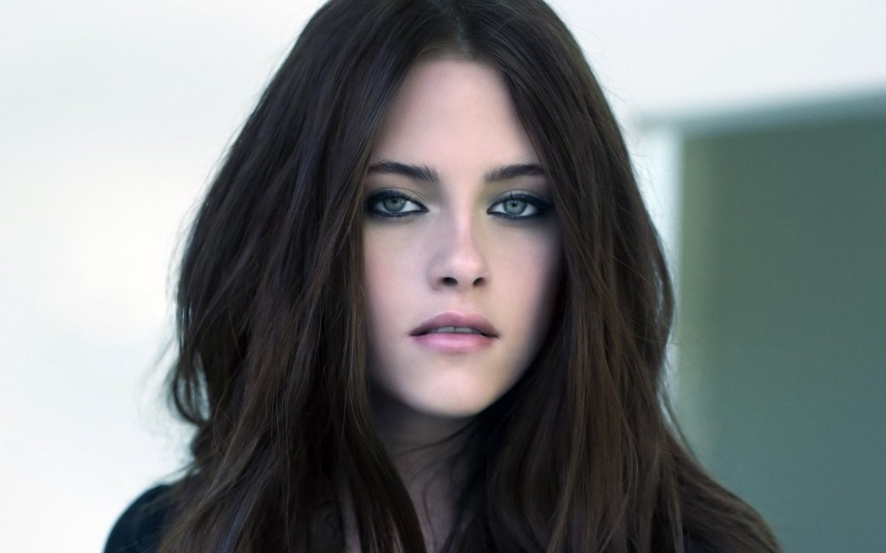A close-up portrait of Kristen Stewart, showcasing her striking features and long, dark hair, set against a softly blurred background.
