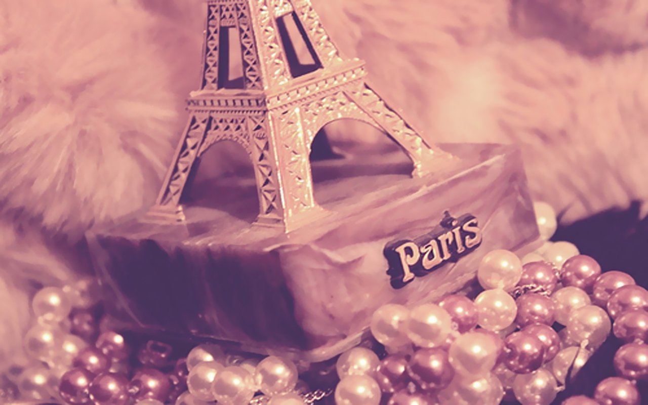 Artistic photography of a miniature Eiffel Tower labeled Paris, surrounded by pink and pearl beads on a plush fur background.