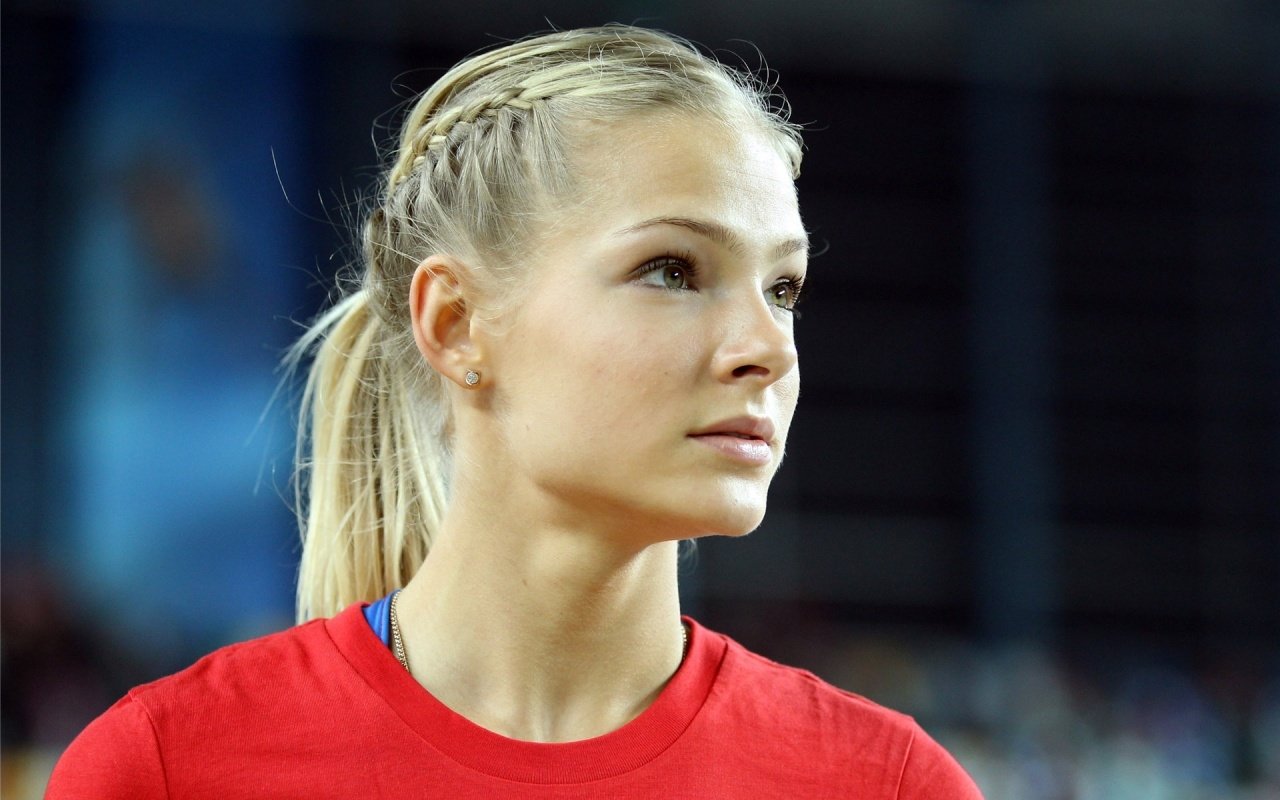 Portrait of athlete Darya Klishina wearing a red sports shirt, focused and preparing for competition in a stadium setting.