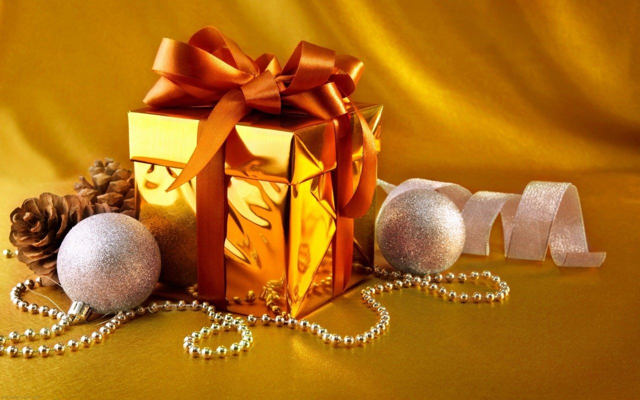 An elegant gold gift box adorned with a vibrant orange ribbon, surrounded by silver ornaments, pine cones, and delicate ribbon on a shimmering yellow background.