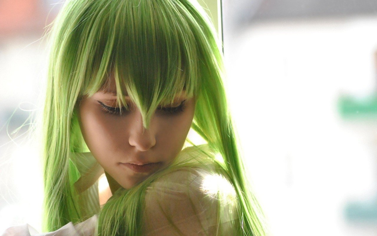 A woman with vibrant green hair gazes downward, her hair flowing elegantly around her shoulders, capturing a moment of serene introspection.