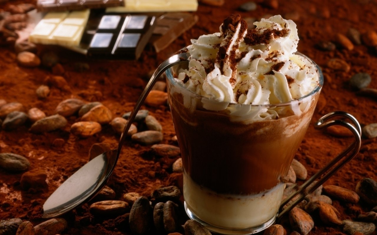 A luxurious iced coffee topped with whipped cream and chocolate shavings, surrounded by cocoa and chocolate bars, highlights a rich and indulgent treat.
