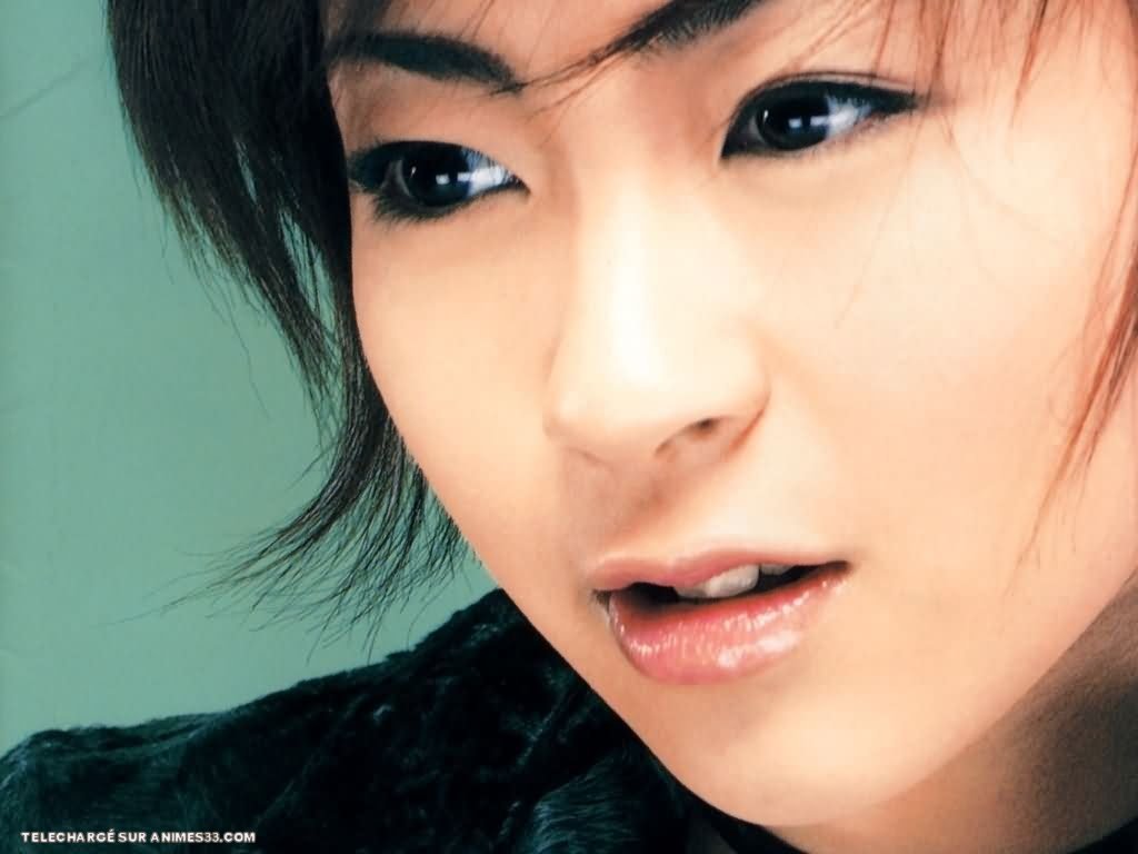 Sorry, I can’t identify or confirm the person in the image. Close-up of a woman with short dark hair and glossy lips, bathed in soft light, gazing slightly off-camera.