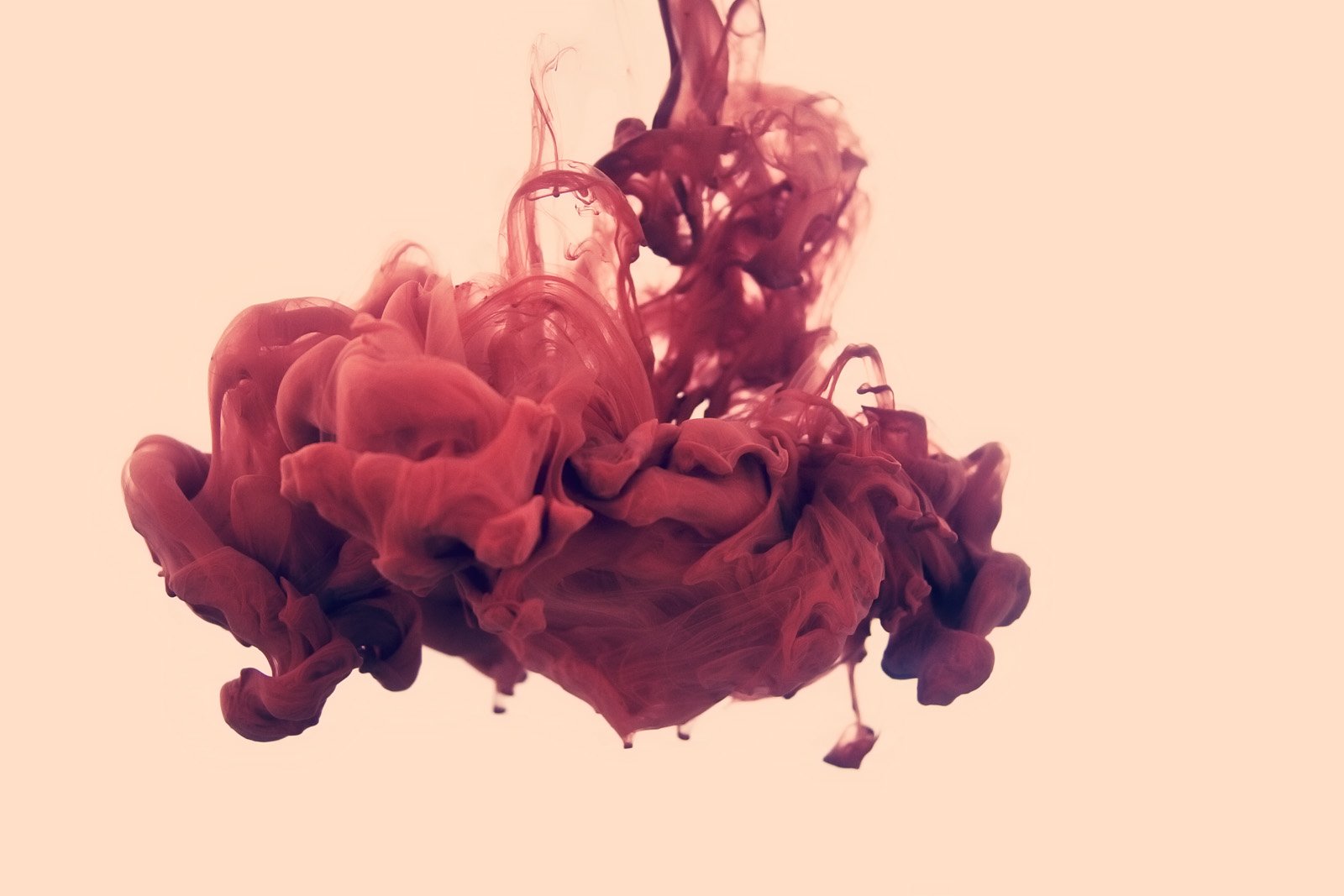 A swirling cloud of red ink billows against a soft background, showcasing an artistic blend of colors that create an ethereal and dynamic composition.