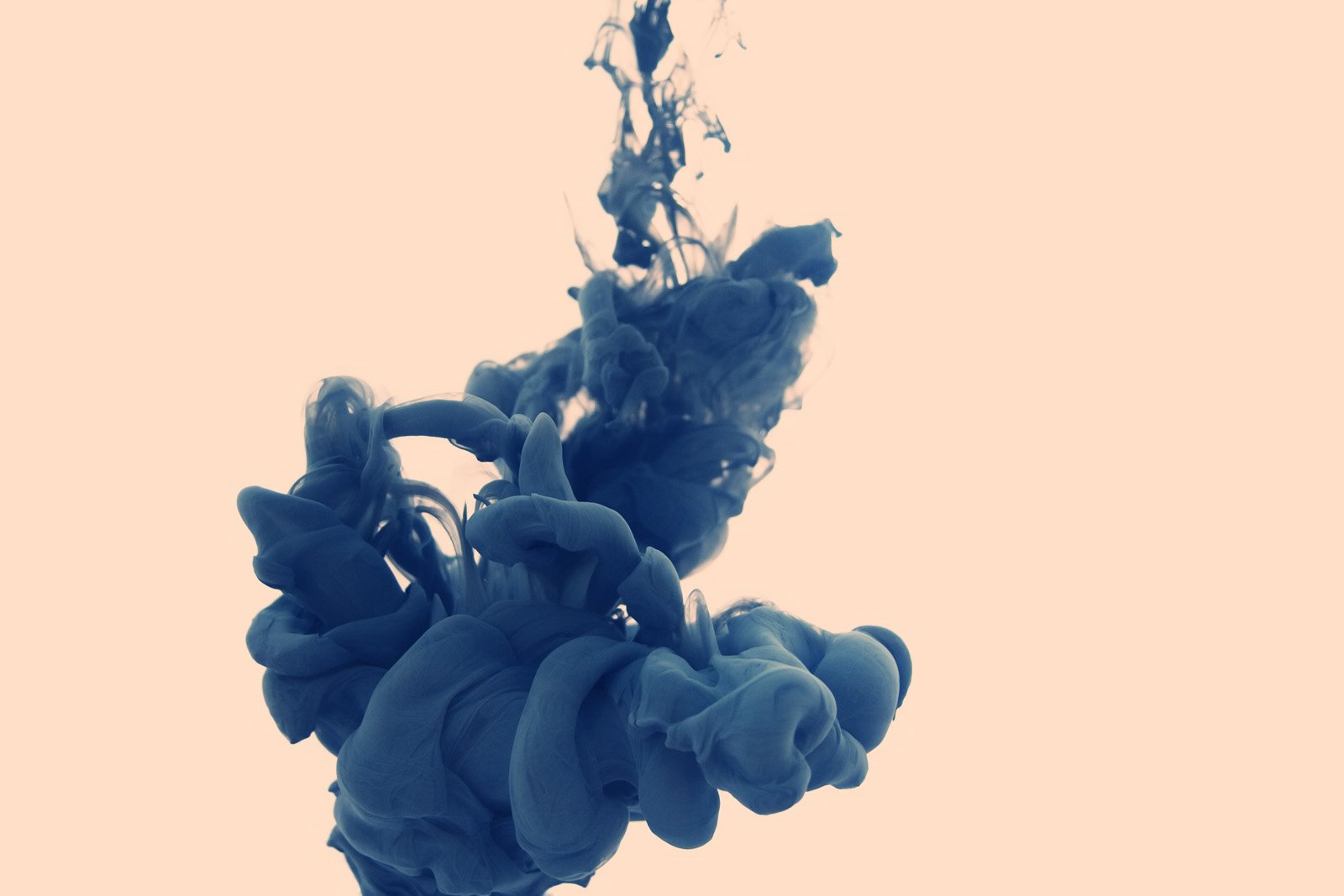 An artistic splash of blue ink swirls gracefully against a soft, pale background, capturing fluid motion and dynamic shapes.