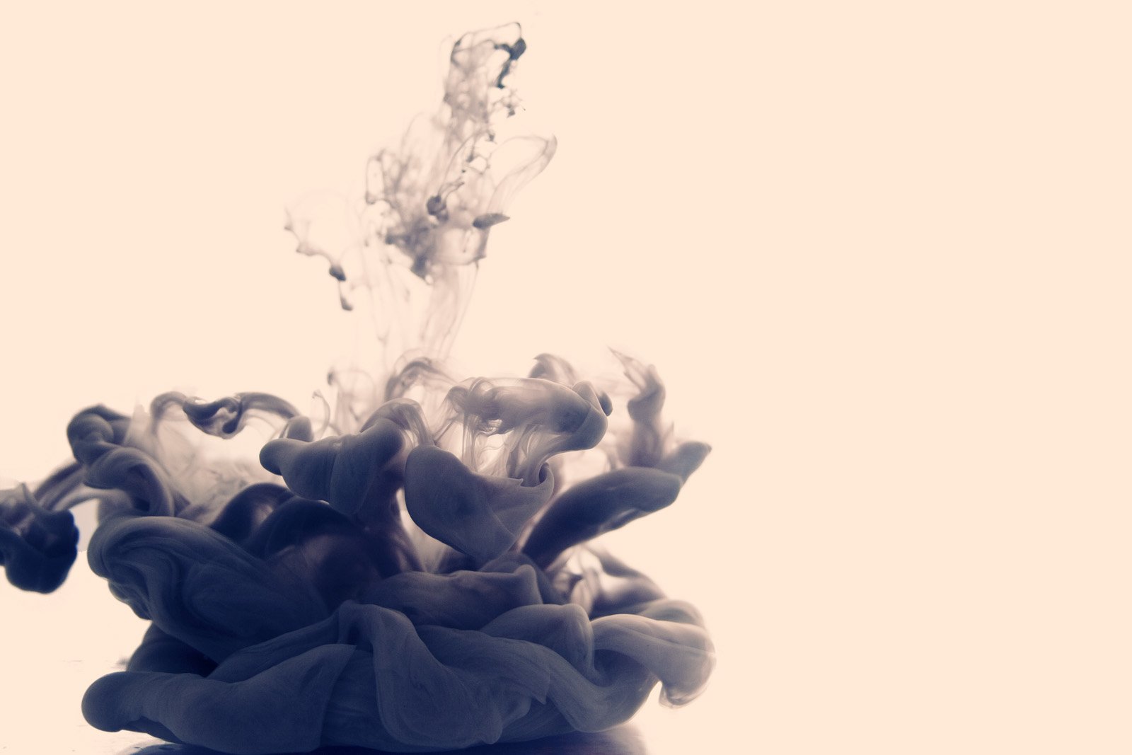 An artistic display of ink swirling gracefully through water, creating intricate patterns against a soft background. The fluid motion evokes a sense of creativity and depth.