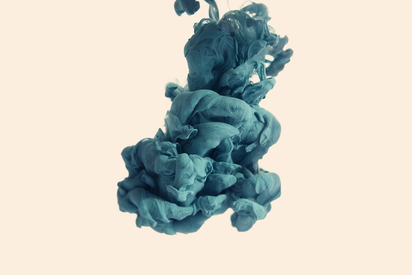 An artistic display of ink swirling in vibrant teal hues against a light background, creating an intriguing abstract composition.