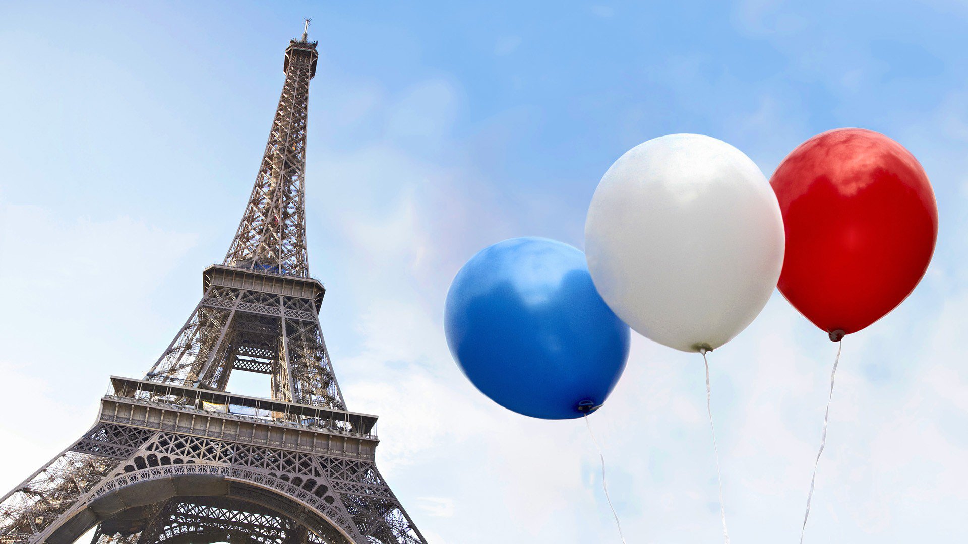 A close-up of the Eiffel Tower stands tall against a blue sky, accompanied by three balloons in blue, white, and red, celebrating the iconic man-made structure.