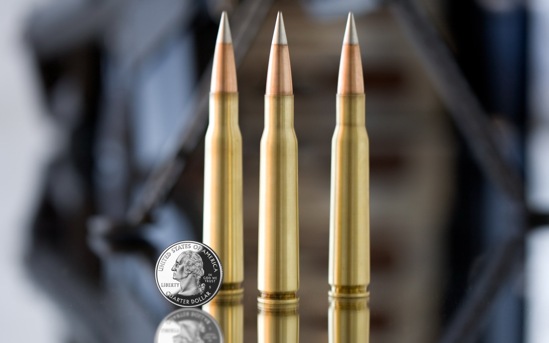 Three man-made bullets standing upright next to a quarter coin on a reflective surface.