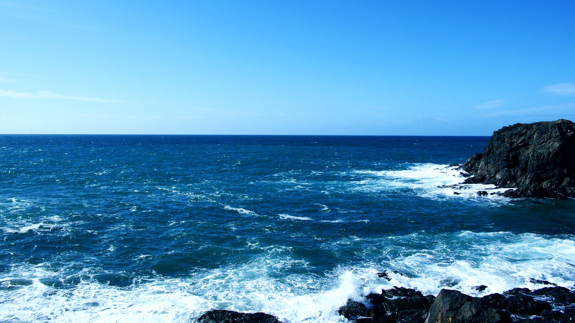 A vibrant seascape showcasing waves crashing against rocky cliffs under a clear blue sky, capturing the beauty of nature.
