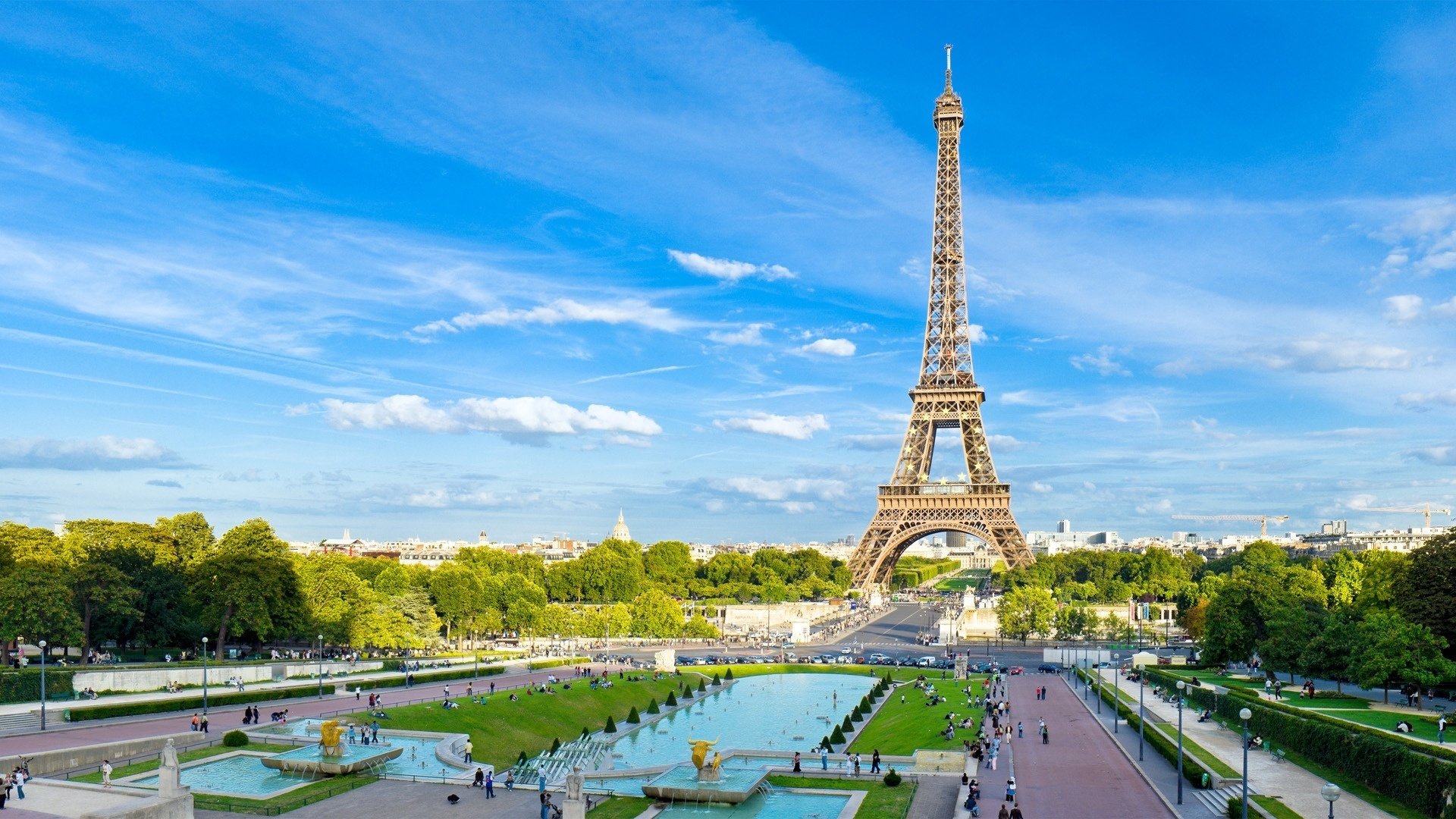 A panoramic view of the Eiffel Tower surrounded by lush greenery and a tranquil fountain, under a clear blue sky, showcasing iconic man-made architecture in Paris.
