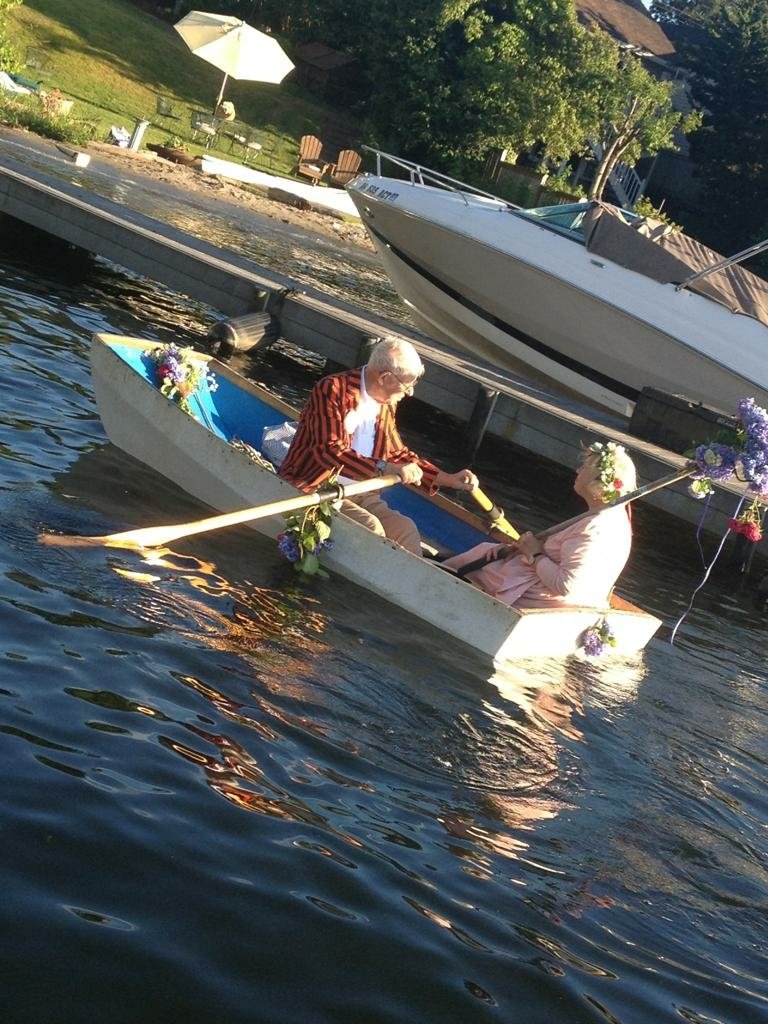 An elderly couple shares a moment in a decorated boat on a serene lake, surrounded by nature, embodying love and connection in this vibrant photography.