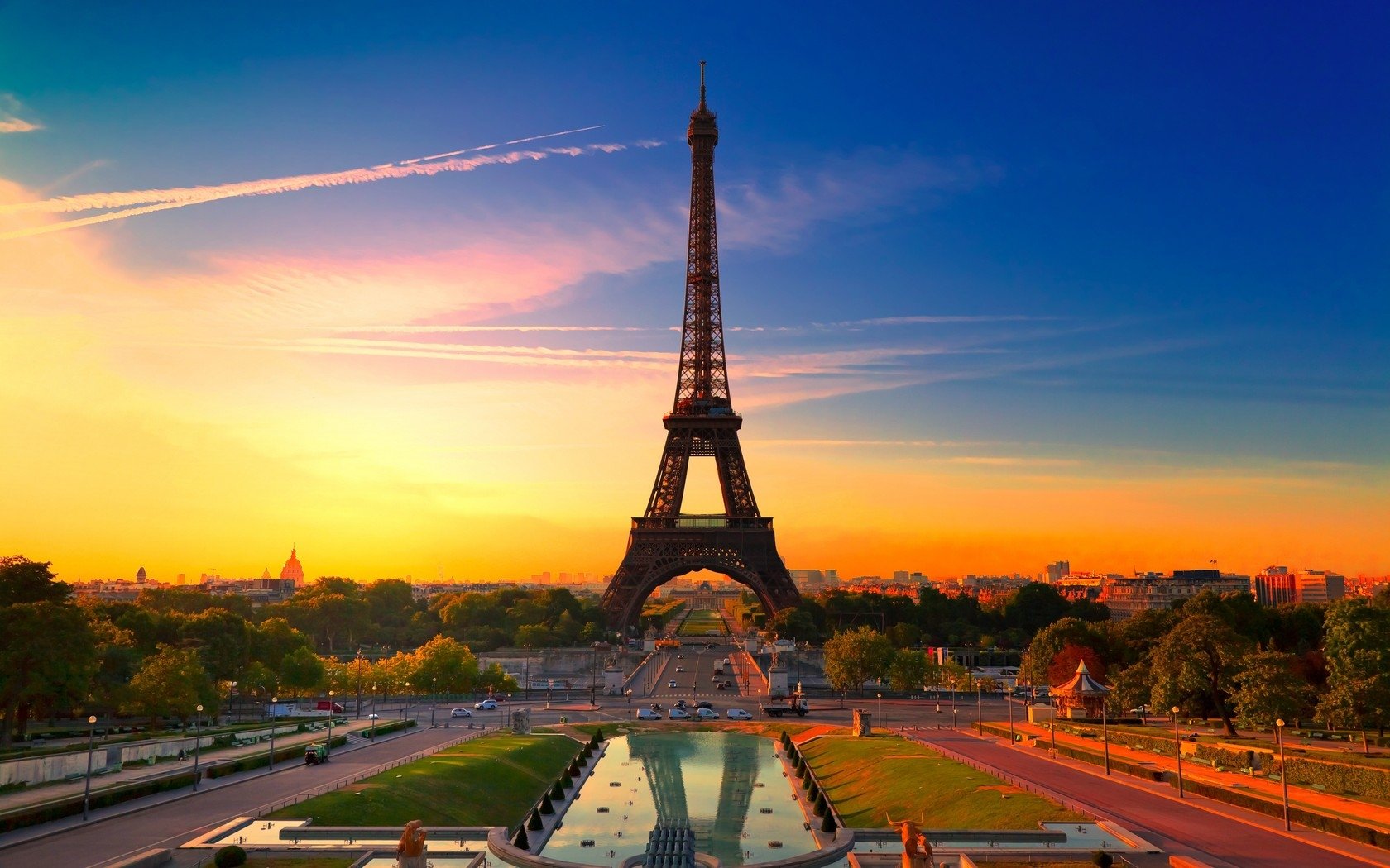 A stunning view of the Eiffel Tower at sunset, surrounded by lush greenery and a tranquil reflecting pool, showcasing the iconic man-made structure against a vibrant sky.