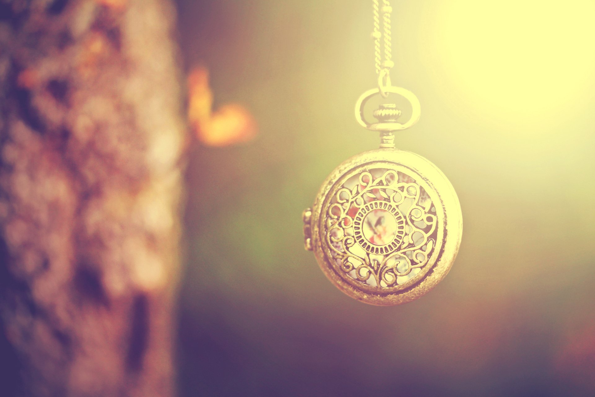 A vintage, intricately designed pocket watch hangs against a softly glowing background, highlighting its man-made craftsmanship and timeless elegance.