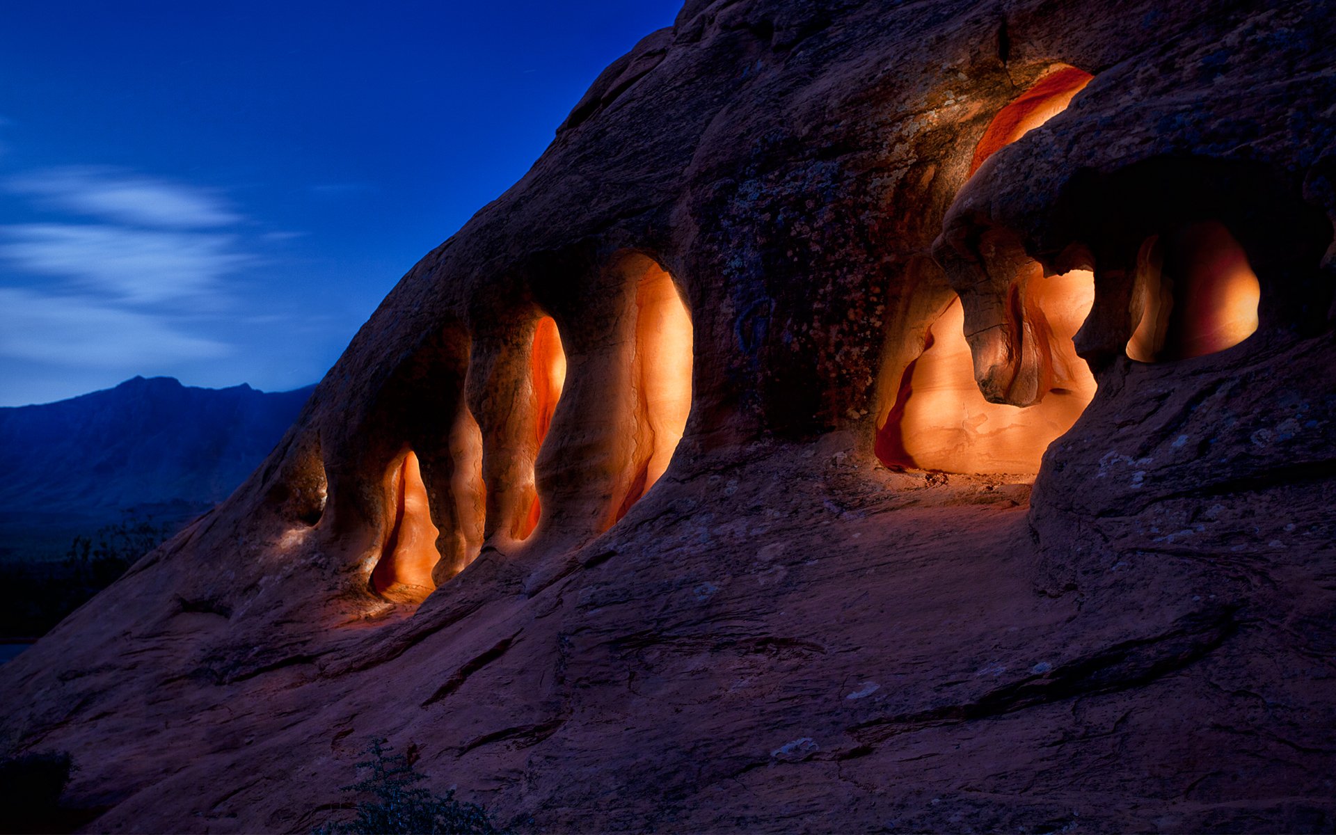 A scenic natural formation features illuminated rock cavities at twilight, showcasing the beauty of the landscape against a twilight sky.