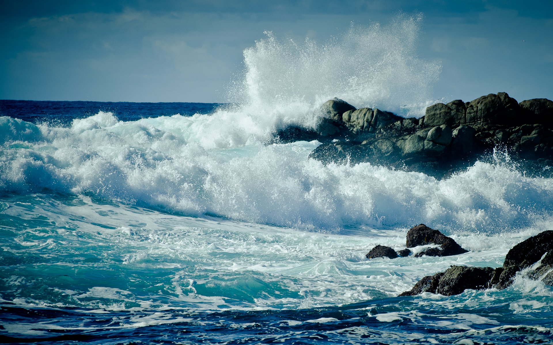 Waves crash against rugged rocks, creating a dynamic scene that captures the beauty of the ocean and the power of nature.