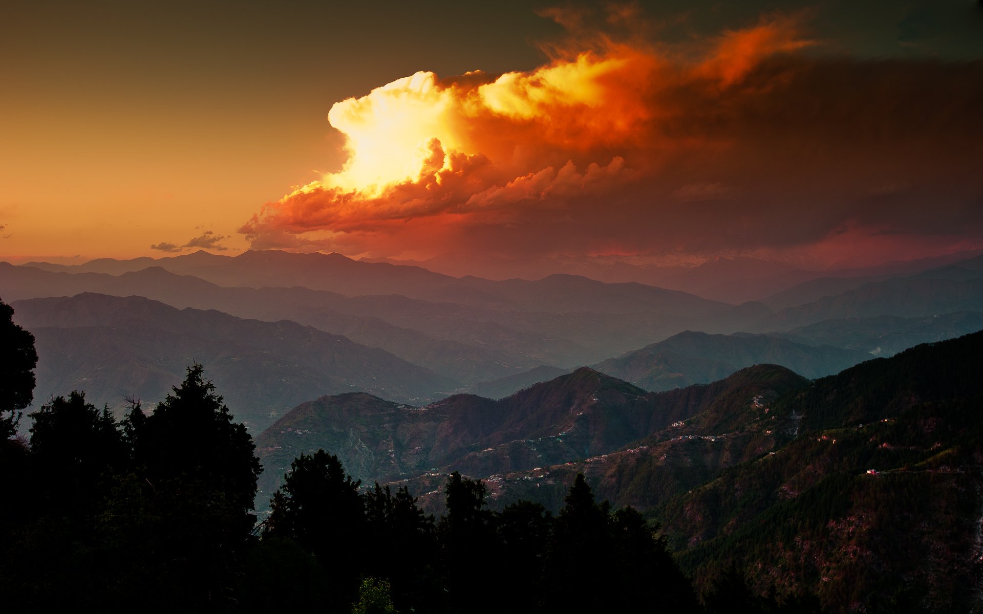 Breathtaking sunset over rolling mountains, illuminated by vibrant orange clouds. Lush silhouettes of trees enhance the serene beauty of this scenic nature landscape.