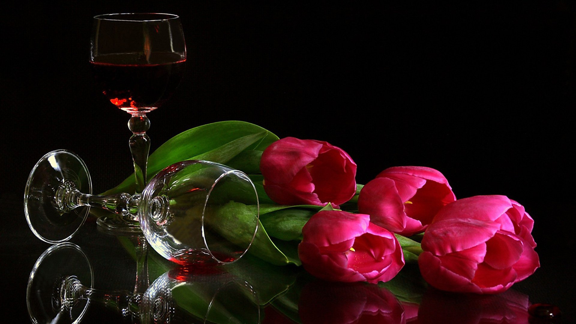 Still life photography featuring vibrant pink tulips and a glass of red wine against a dark background, creating a dramatic and elegant composition.