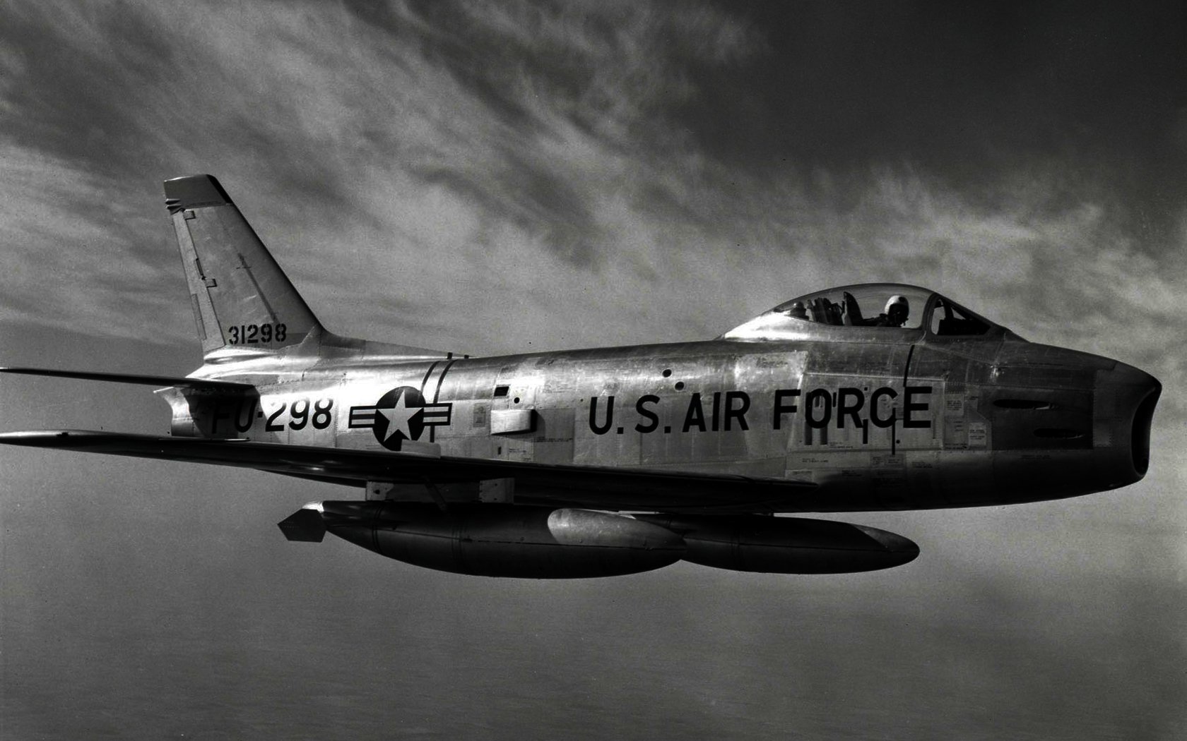 A North American F-86 Sabre flies through the sky, showcasing its sleek design and U.S. Air Force markings against a dramatic backdrop of clouds.