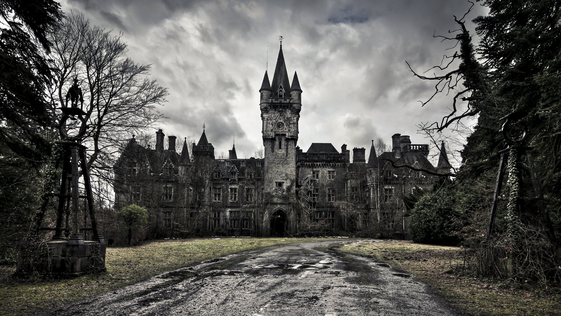 Gothic man-made stone castle with a central spired tower, brooding clouds overhead, overgrown grounds and a cracked driveway leading to an arched entrance.