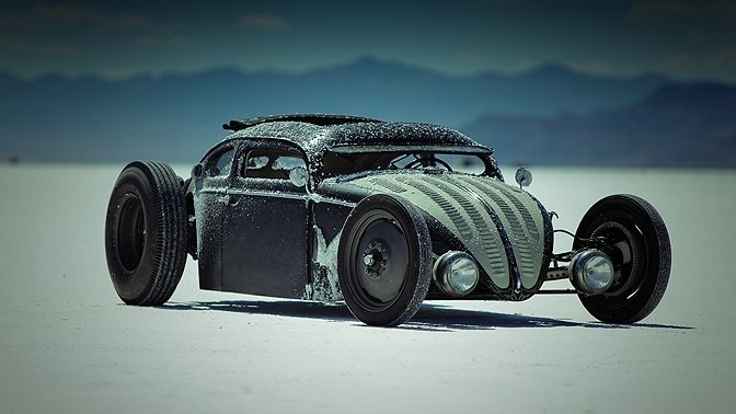 Low-slung Volkswagen vehicle — a chopped-roof Beetle rat rod with exposed wheels and weathered metal finish parked on white salt flats with distant mountains.