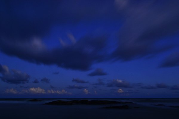 Dark blue sky with scattered clouds above a calm natural landscape at dusk.