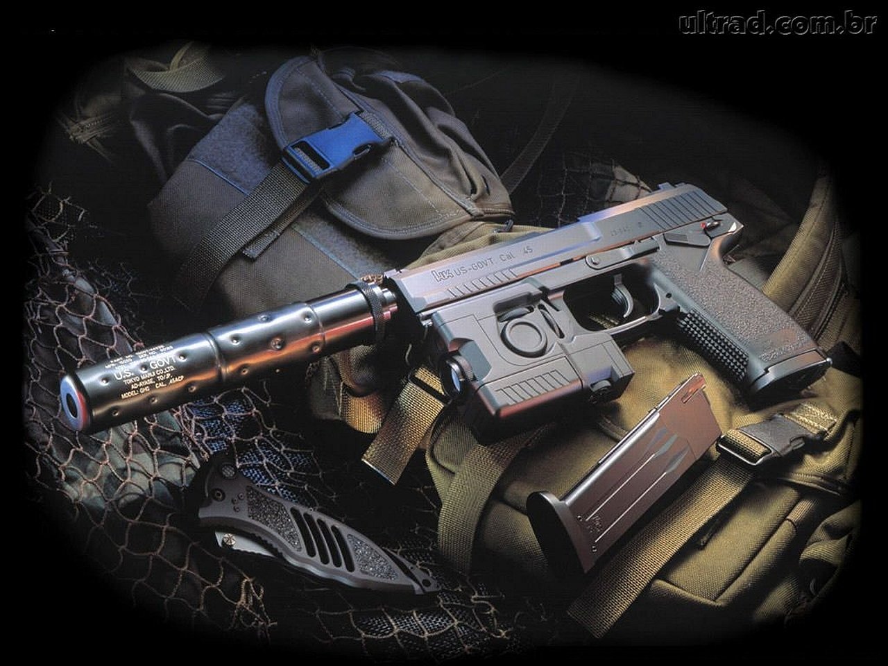 A hand gun with a suppressor rests on a tactical background, surrounded by gear and a magazine, highlighting a focused display of man-made firearm equipment.