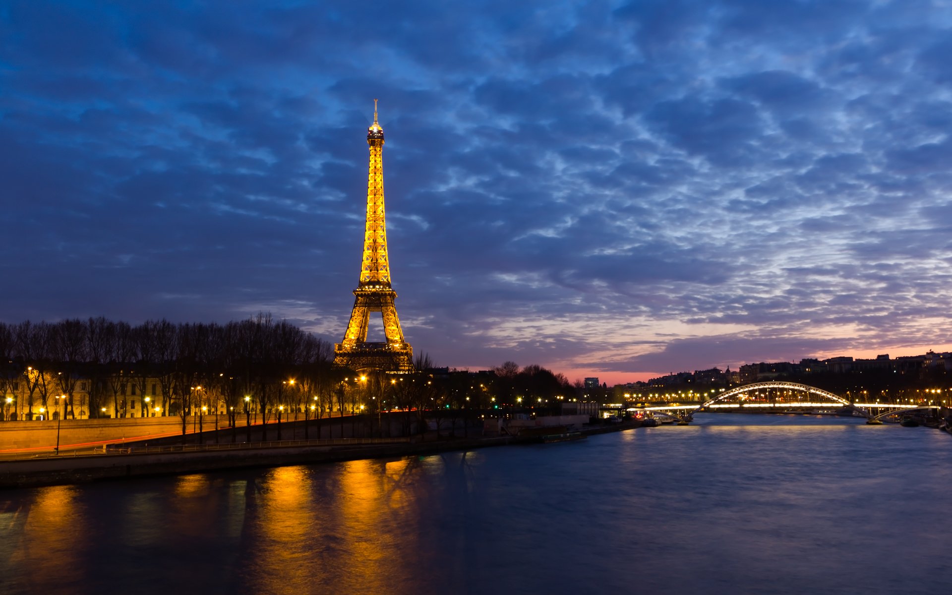 The image captures the illuminated Eiffel Tower at dusk, reflecting over the Seine River, with a beautiful twilight sky enhancing the iconic man-made structure's charm.