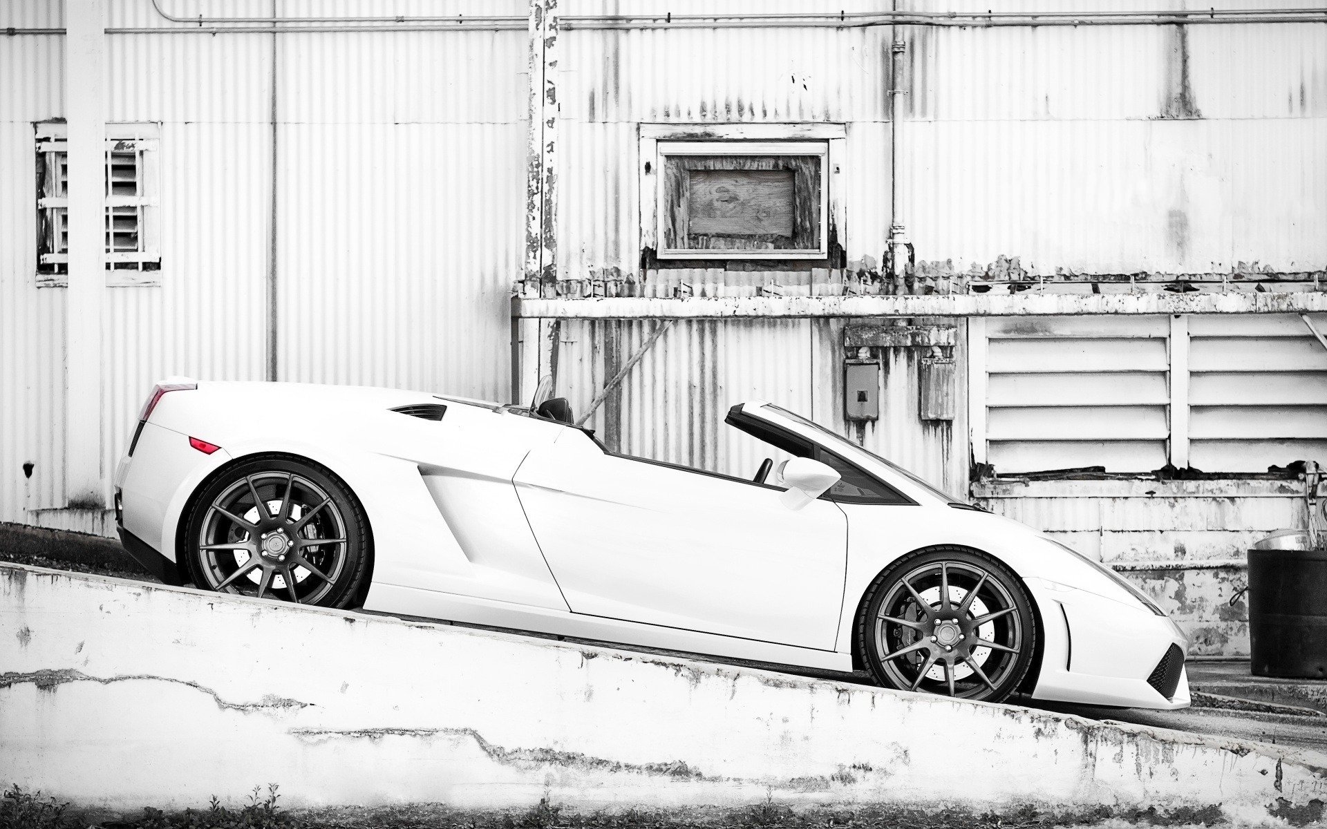 A sleek white Lamborghini Gallardo parked on an incline against a backdrop of industrial structures, showcasing its sporty design and elegant lines.