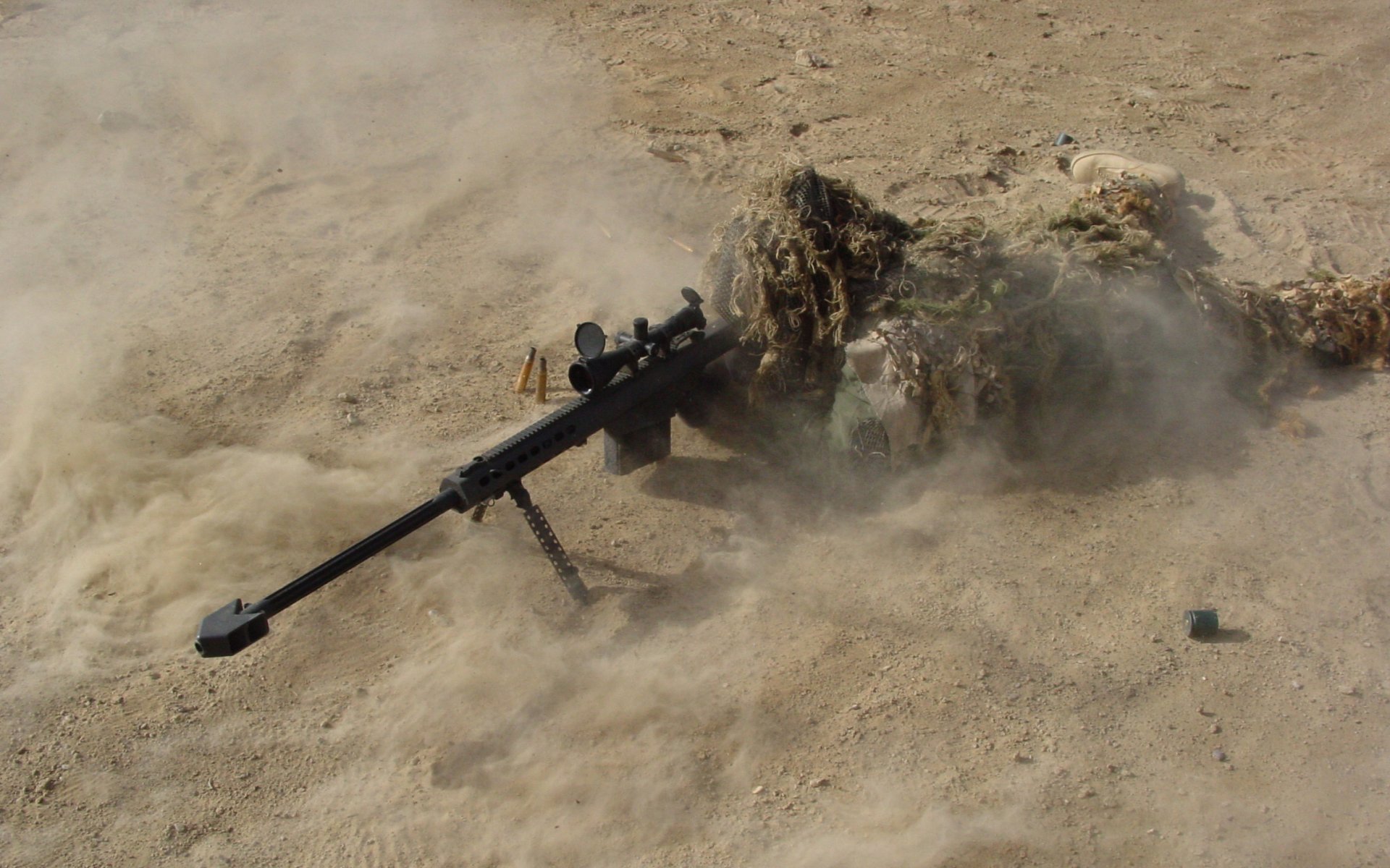A military sniper camouflaged in terrain, lying low with a sniper rifle positioned beside them, surrounded by dust and debris.