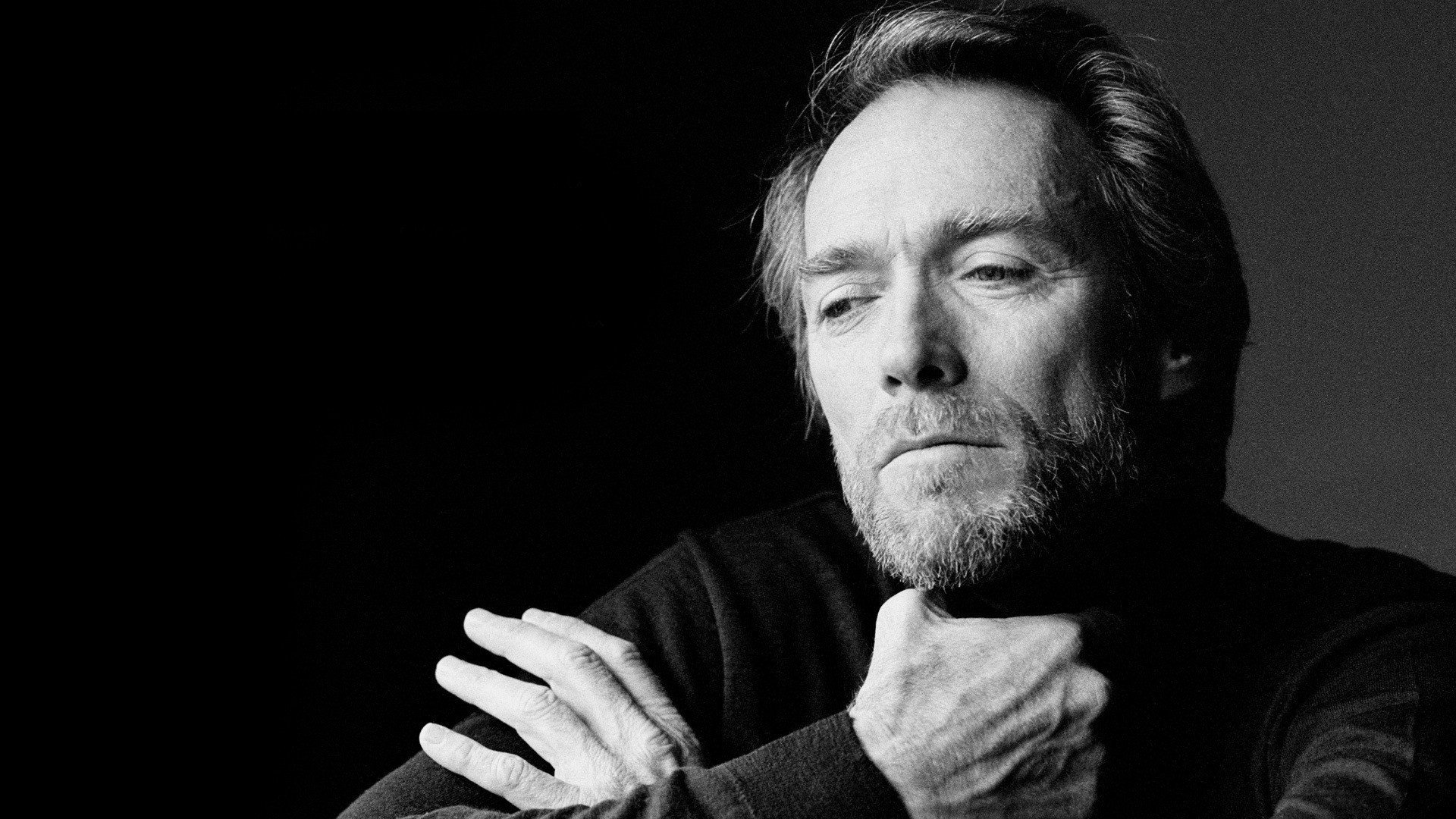 A black and white portrait of celebrity Clint Eastwood, gazing thoughtfully while resting his chin on his hand, conveying a sense of introspection.