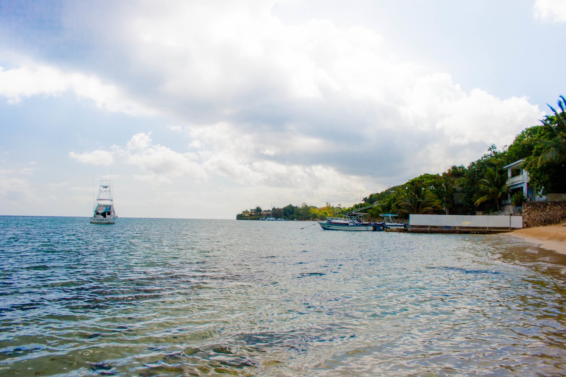 Photography captures a serene ocean scene with calm waters, a distant boat, and a tree-lined shore under a partly cloudy sky.