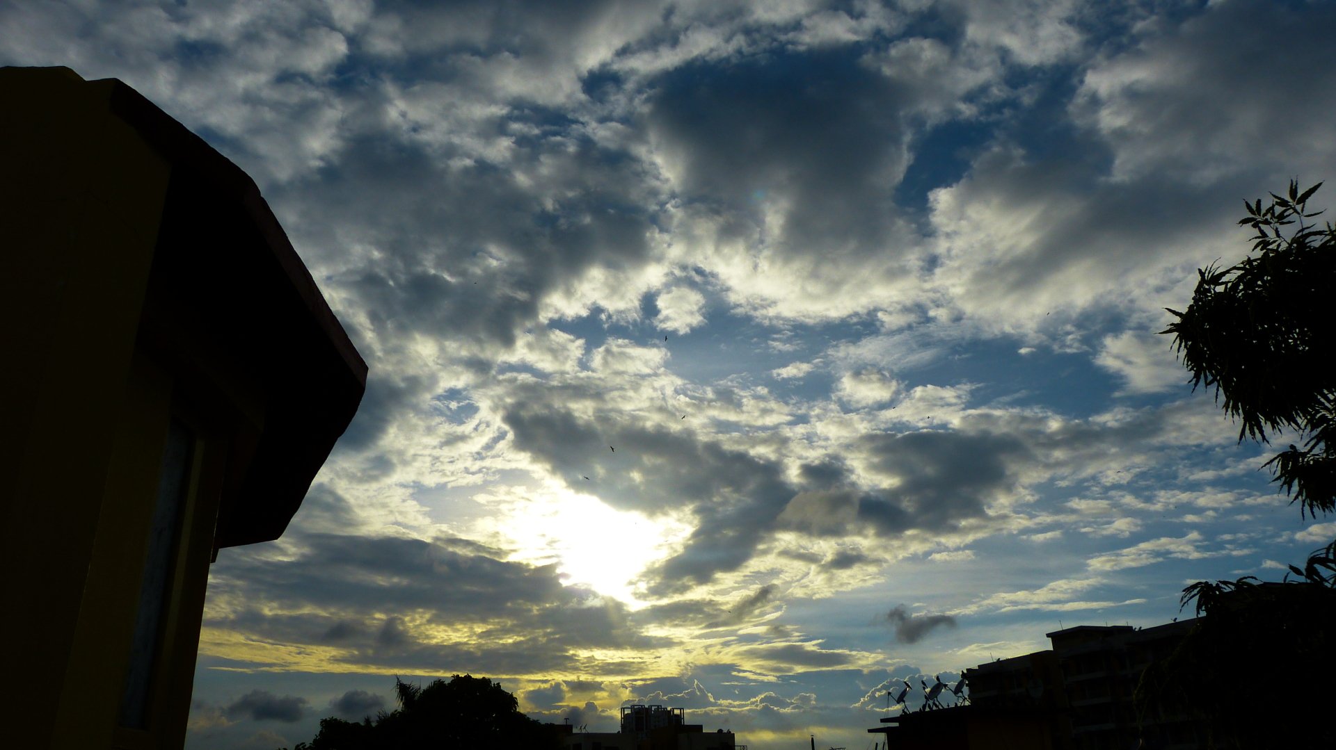 A vibrant sky filled with scattered clouds above silhouetted natural and urban elements.