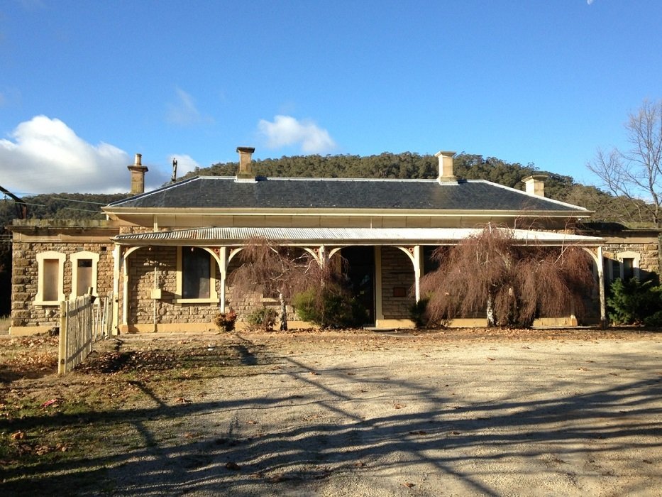 Historic man-made train station building with a stone facade, arched entryways, and a dark roof set against a clear blue sky and natural landscape.