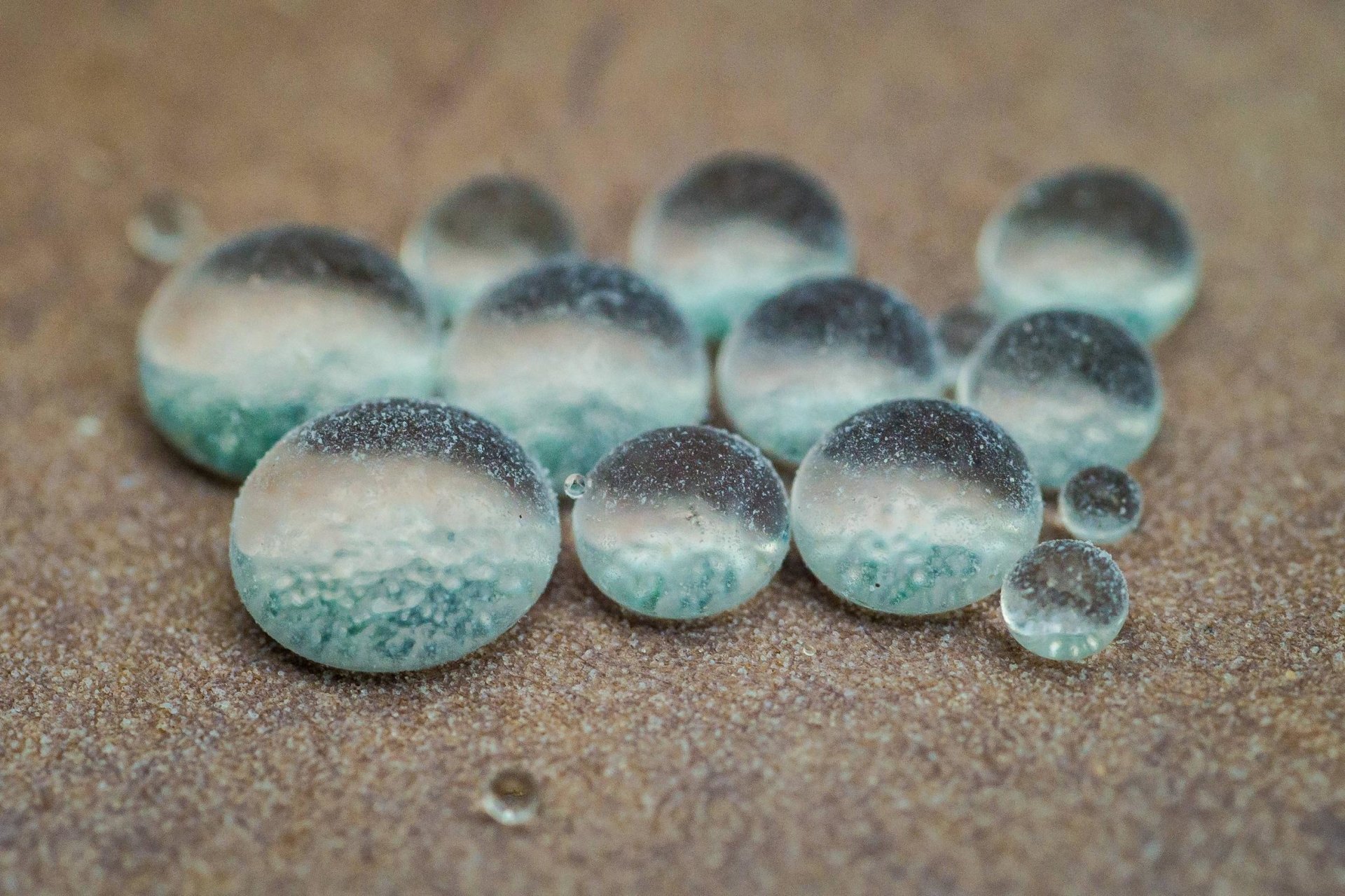A close-up of various water drops resting on a surface, showcasing delicate reflections and subtle colors, highlighting the beauty of nature.