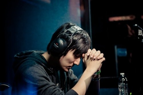 Esports gamer in headset concentrating on the video game StarCraft, hands clasped and head bowed at a tournament station.