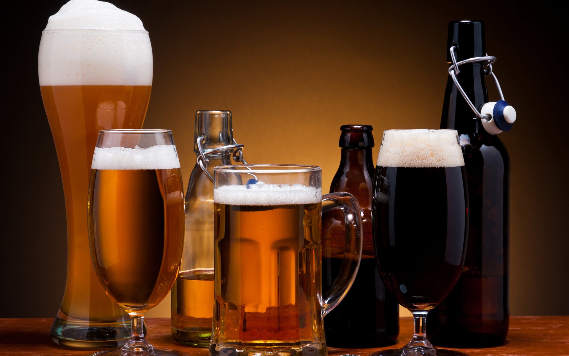 Assortment of beers — light, amber, and dark — in bottles and glasses on a wooden table, food and beer theme against a warm brown backdrop.
