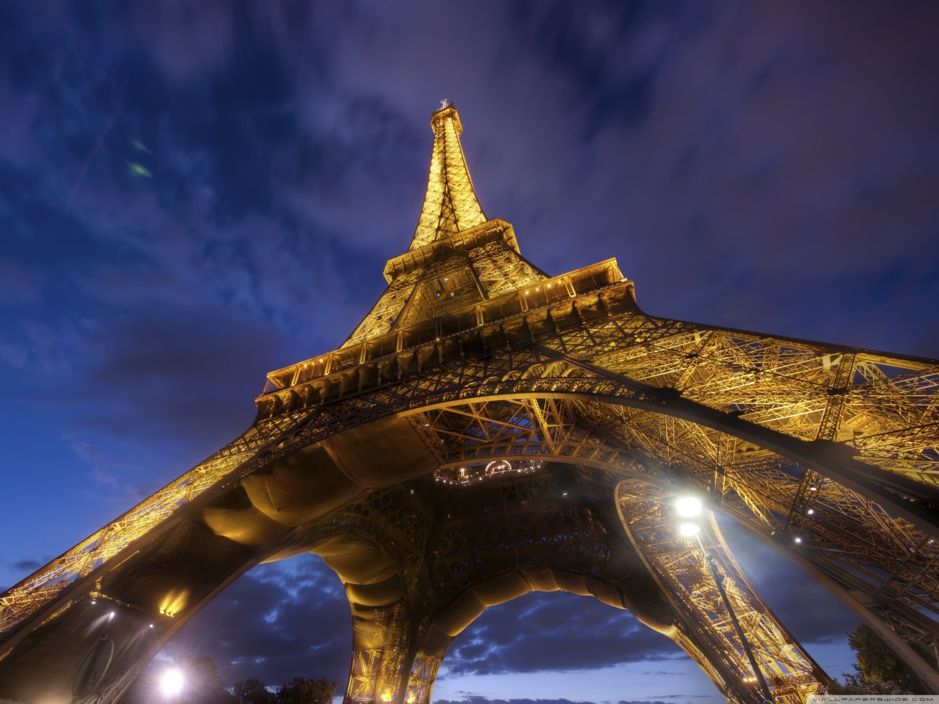 A stunning view of the Eiffel Tower illuminated against a twilight sky, showcasing its intricate ironwork and grandeur from below.