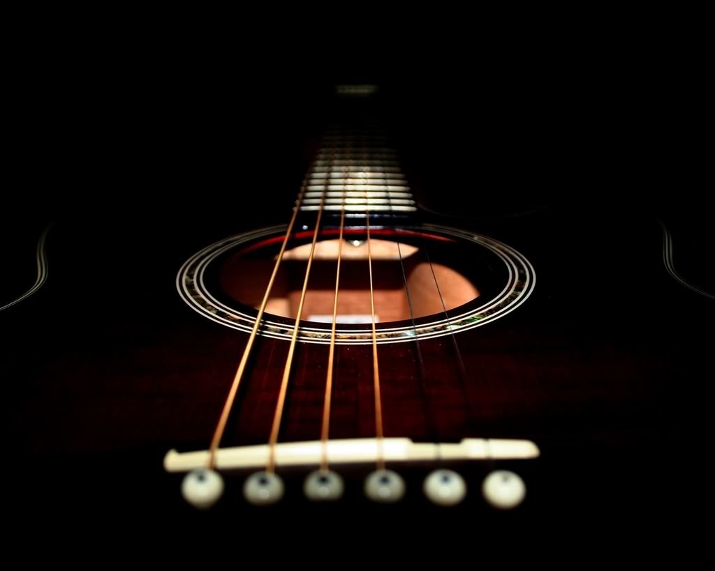 Close-up of a guitar, showcasing its strings and sound hole against a dark background, highlighting the artistry of music.