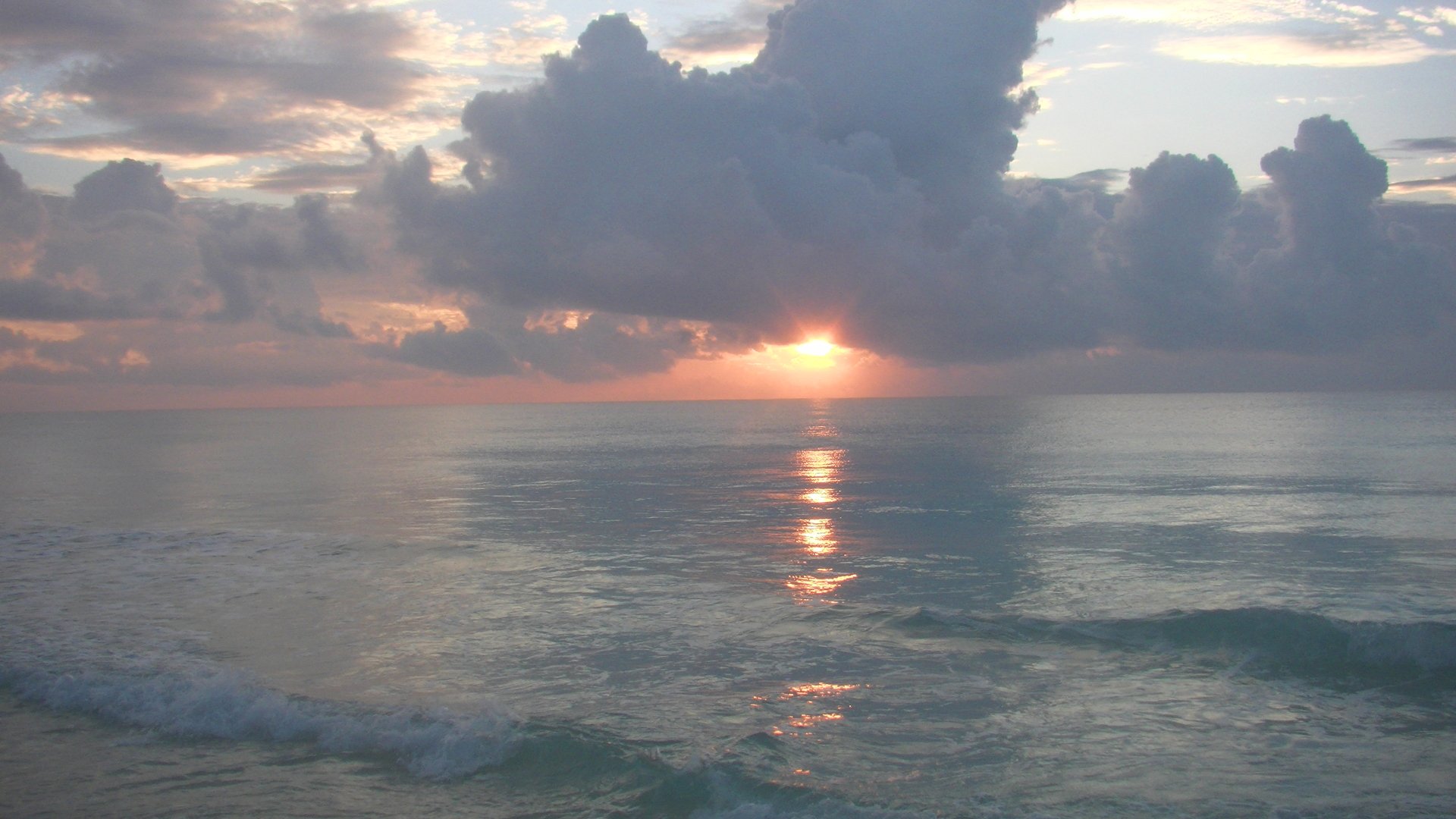 A tranquil sunrise over the ocean in Cancún, Mexico, with soft clouds reflecting the warm colors of dawn on the still water.