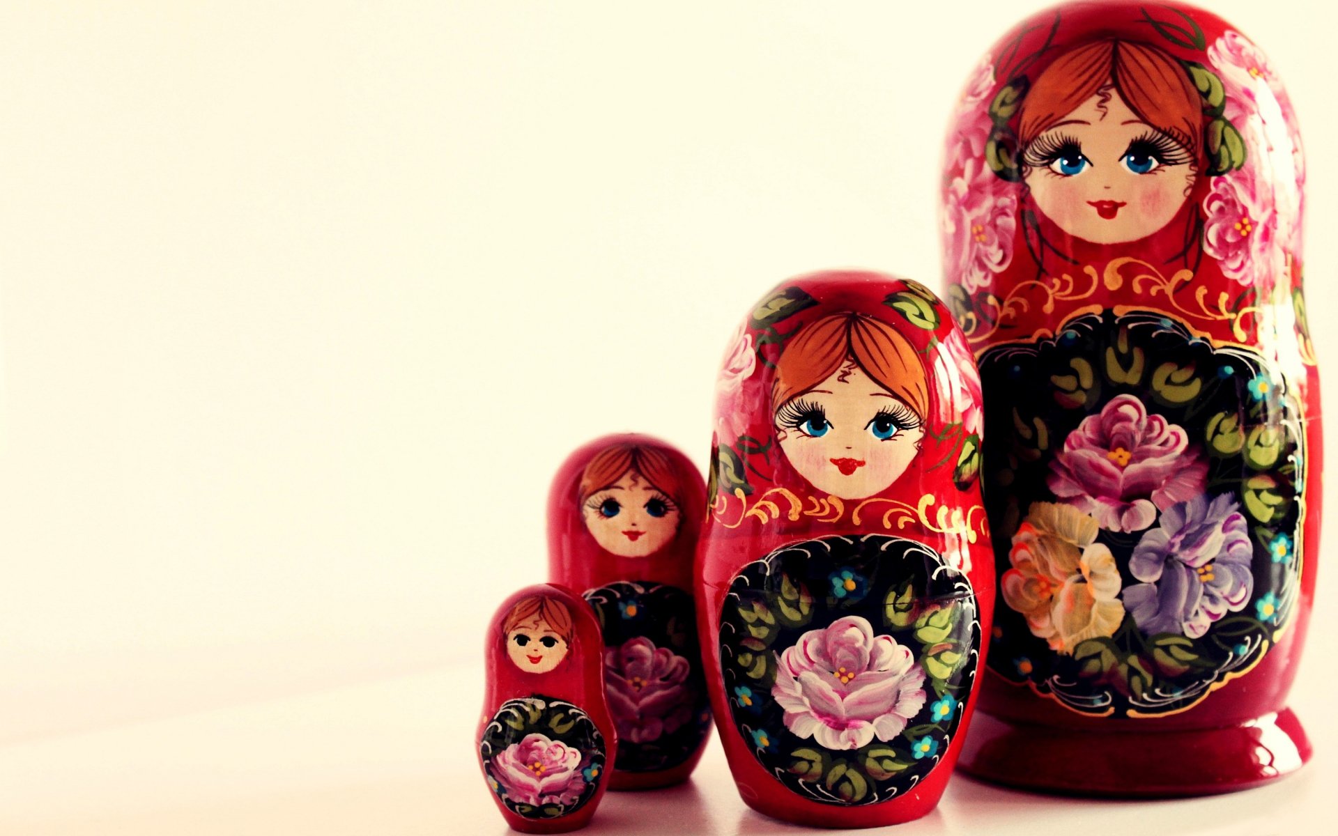 Line of man-made nesting dolls (matryoshka) painted red with floral designs, arranged from largest to smallest on a pale background.