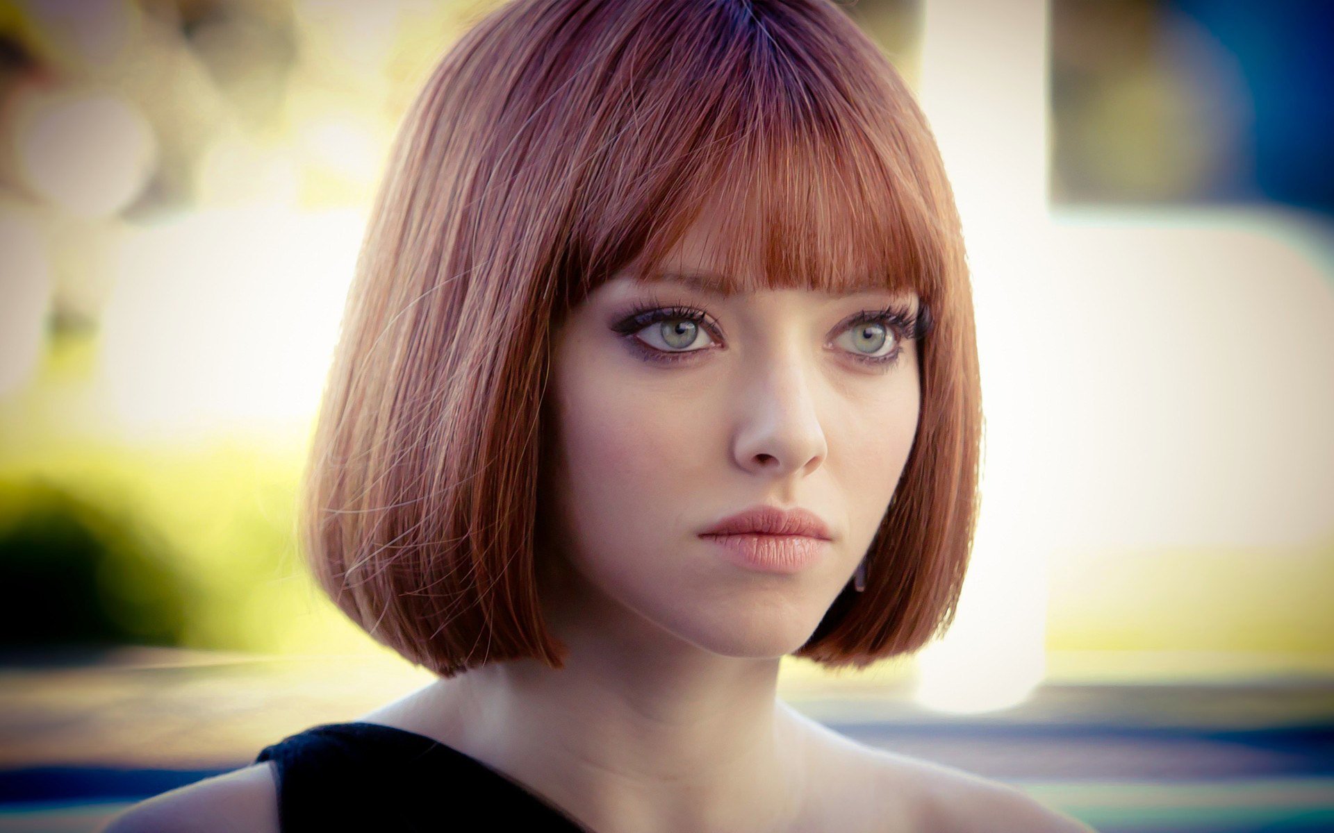 I don't know who this is. Woman with auburn bob and bangs, green-blue eyes, solemn expression, sleeveless black top, blurred outdoor background.